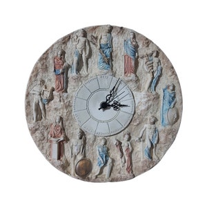 May include: A round, beige-colored wall clock with a white face and black hands. The clock features a decorative design of Greek gods and goddesses around the outer edge. The clock face has the names of the gods and goddesses written in Greek around the outer edge.