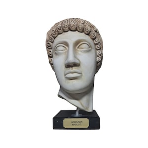 Könnte beinhalten: Weiße Gipsbüste des griechischen Gottes Apollon auf einem schwarzen Sockel mit einer goldenen Plakette mit der Aufschrift "ΑΠΟΛΛΩΝ APOLLO".