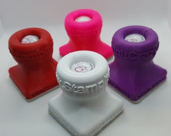 Pode incluir: Quatro prensas de carimbo coloridas em vermelho, rosa, branco e roxo. Cada prensa tem uma base quadrada e um topo cilíndrico com o texto "StampitCrazy" e "Crazy Press". As prensas de carimbo são projetadas para artesanato e scrapbooking.