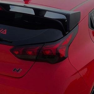 May include: A red car with a black rear spoiler and blacked-out taillights. The taillights have a heart-shaped design. The car has a "N" logo on the back.