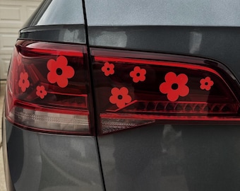 May include: A gray car with red flower decals on the taillight. The decals are in the shape of simple flowers with five petals.