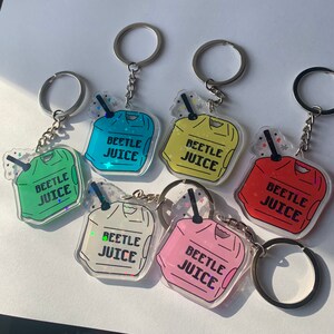 May include: A collection of six acrylic keychains in various colors, each featuring a cartoon-style beverage container design. The keychains have the text "BEETLE JUICE" printed on them, and are attached to silver key rings.