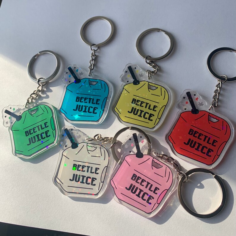 May include: A collection of six acrylic keychains in various colors, each featuring a cartoon-style beverage container design. The keychains have the text "BEETLE JUICE" printed on them, and are attached to silver key rings.