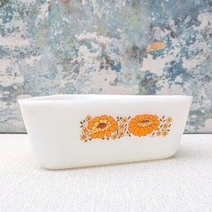 May include: White rectangular baking dish with a floral design featuring orange and yellow flowers. The dish has a white background with a brown outline around the flowers.