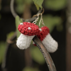 May include: Crocheted mushroom earrings with red caps and white stems hanging from a metal hook.