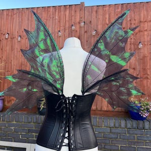 May include: Black leather corset with a lace-up back, worn with a pair of large, green and black fairy wings.
