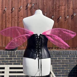 May include: A black leather corset with a lace-up back, worn on a white mannequin. The mannequin is wearing pink fairy wings.