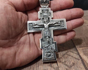 May include: A silver cross pendant with intricate details, featuring a depiction of Jesus Christ on the cross. The cross has a detailed design with various symbols and inscriptions.