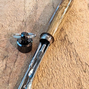 May include: A wooden carrying case with a metal cap and a keychain ring. The case is open and contains several metal tools with different tips.