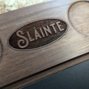 May include: A wooden serving tray with a circular cutout and the word "Sl&aacute;inte" engraved in the center. The tray has a dark brown wood finish.