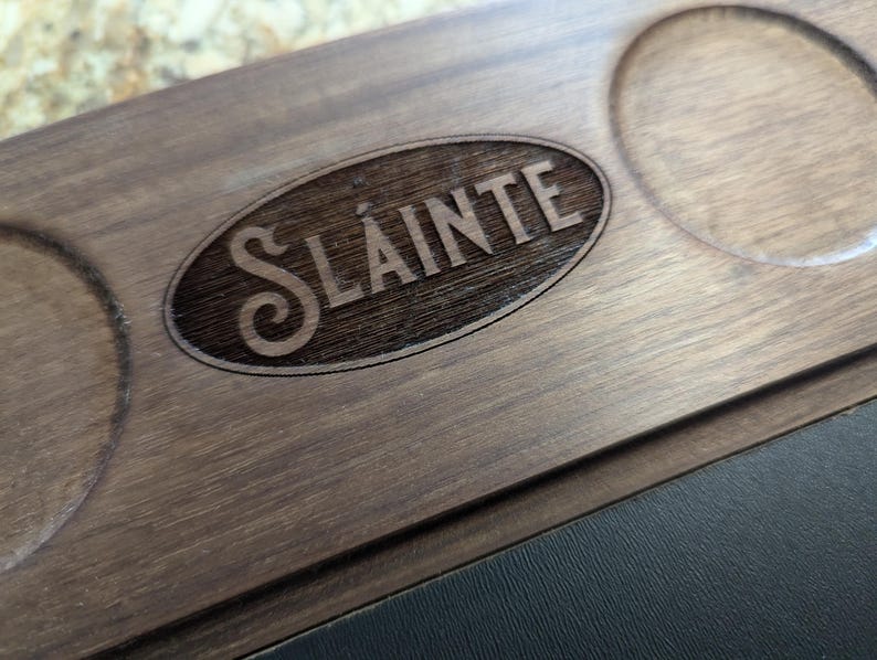 May include: A wooden serving tray with a circular cutout and the word "Sl&aacute;inte" engraved in the center. The tray has a dark brown wood finish.