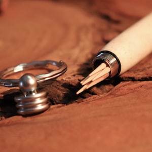 May include: A white wooden toothpick holder with a silver metal top and a silver metal ring. The holder is open and toothpicks are visible inside.
