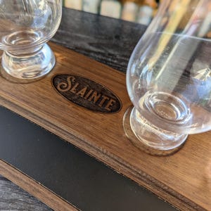 May include: A wooden serving tray with a black inlay and the word "Slainte" engraved on it. Two clear glass whiskey glasses are on the tray.