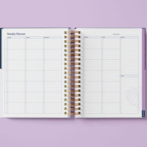 May include: An open weekly planner with a blue cover and gold spiral binding. The planner has a white interior with lined pages for daily scheduling.