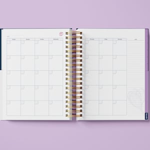 May include: An open, spiral bound planner with a blue and purple cover. The planner has a weekly layout with a notes section on the right side. The planner has a gold spiral binding.