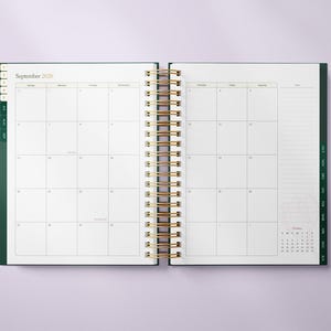 May include: Open planner with a gold spiral binding, displaying the September 2026 calendar. The planner has a dark green cover and tabs, with a small October calendar at the bottom right. The pages are white with a grid layout.