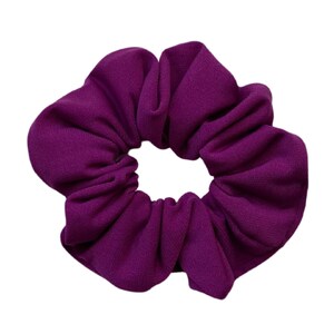 May include: A purple scrunchie made of soft fabric. The scrunchie is gathered and bunched to create a round shape.