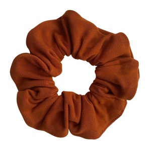 May include: A brown scrunchie made of soft fabric. The scrunchie is gathered and tied into a circle shape.