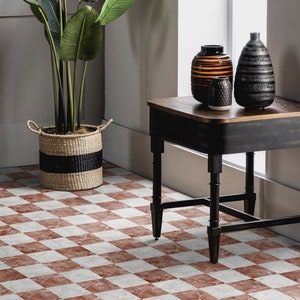 Peut inclure: Une table d'appoint noire avec un plateau en bois et trois pieds. La table est décorée de trois vases, un brun et rayé, un noir et rayé et un petit, rond et texturé. La table est posée sur un sol en damier avec des carreaux rouges et blancs.
