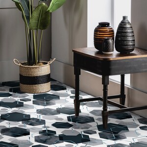 Peut inclure: Une table d'appoint noire avec un plateau en bois et trois pieds. La table est décorée de trois vases, un brun, un noir et blanc et un petit blanc. La table est posée sur un sol avec un motif géométrique bleu et gris.