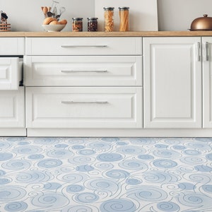 Peut inclure: Des armoires de cuisine blanches avec des tiroirs et des portes, avec un plan de travail en bois clair. Le sol est recouvert d'un carrelage en vinyle bleu et blanc.