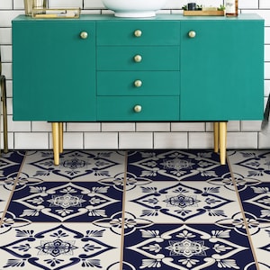 May include: A teal cabinet with gold legs sits in front of a white metro tile wall. The cabinet has three drawers and two doors. The floor is covered in blue and white patterned tile.