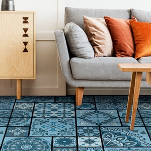 Puede incluir: Un sofá gris con cojines naranja y beige se encuentra sobre un suelo de baldosas con estampado azul y blanco. Una mesa de café de madera con un jarrón de flores se encuentra frente al sofá.