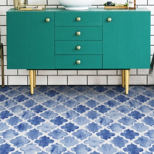 May include: A teal blue cabinet with gold hardware sits on a blue and white patterned tile floor. The cabinet has four drawers and two doors.