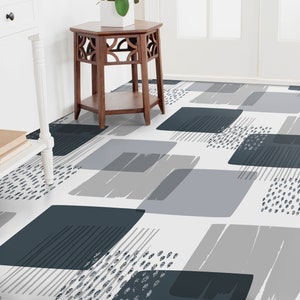 Puede incluir: Una alfombra geométrica con estampado blanco, gris y azul con formas abstractas y puntos negros. La alfombra está colocada en un pasillo con una mesa de madera y una pared blanca.