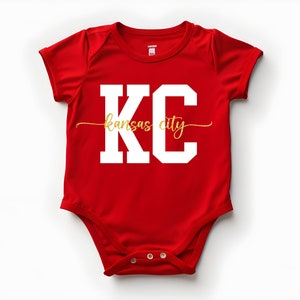 May include: Red baby onesie with white lettering that says "KC Kansas City" in a gold script font.