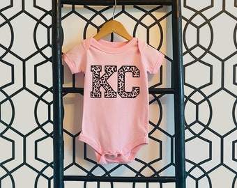 May include: Pink baby onesie with a black and white leopard print "KC" graphic.