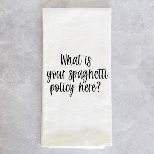 May include: White kitchen towel with black text that reads "What is your spaghetti policy here?"