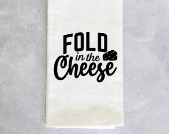 May include: White kitchen towel with black text that reads "Fold in the Cheese" with a small black cheese wedge graphic.