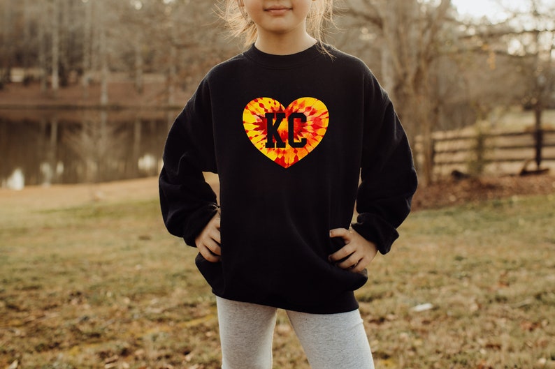 May include: Black sweatshirt with a tie-dye heart design featuring the letters "KC" in black.