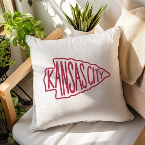 May include: White throw pillow with a red arrow design that says "KANSAS CITY" in a handwritten font.
