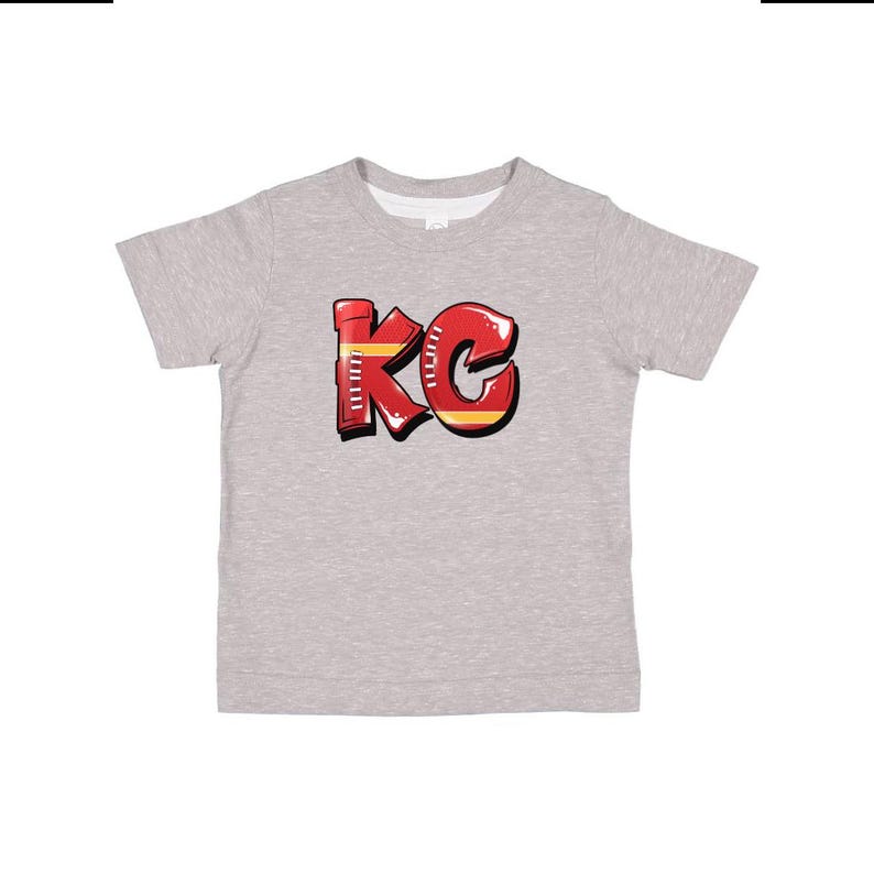 May include: A heather grey t-shirt with a red and yellow graphic of the letters "KC" in a graffiti style.
