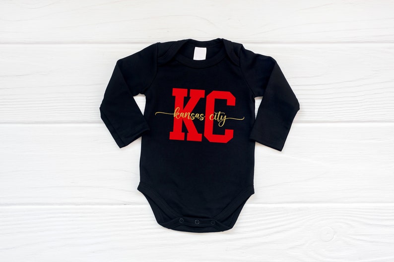 May include: Black long-sleeve baby onesie with red "KC" lettering and gold "kansas city" text.