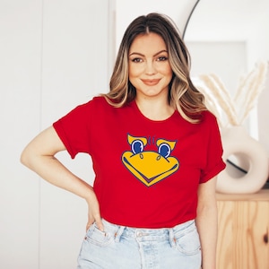 May include: A red t-shirt with a yellow and blue cartoon bird mascot on the front. The bird has large blue eyes and a yellow beak.