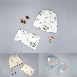 Könnte beinhalten: Drei Sets mit passenden Baby-Mützen und Stirnbändern. Das erste Set besteht aus einer weißen Mütze und einem weißen Stirnband mit einem Waschbär-Druck. Das zweite Set besteht aus einer braunen und beigefarbenen Mütze und einem Stirnband mit einem Eichhörnchen-Druck. Das dritte Set besteht aus einer blauen Mütze und einem blauen Stirnband mit einem Fuchs-Druck.