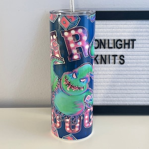 Puede incluir: Un vaso de acero inoxidable azul y verde con un gr&aacute;fico de un monstruo verde con la boca cosida y las palabras "Oogie Boogie" en luces rosas y blancas. El vaso tiene una tapa transparente y una pajita plateada.