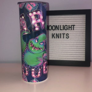 Puede incluir: Un vaso azul y verde con un gr&aacute;fico de un personaje de la pel&iacute;cula "Pesadilla antes de Navidad". El personaje est&aacute; rodeado de luces rosas y blancas que deletrean "Boo".