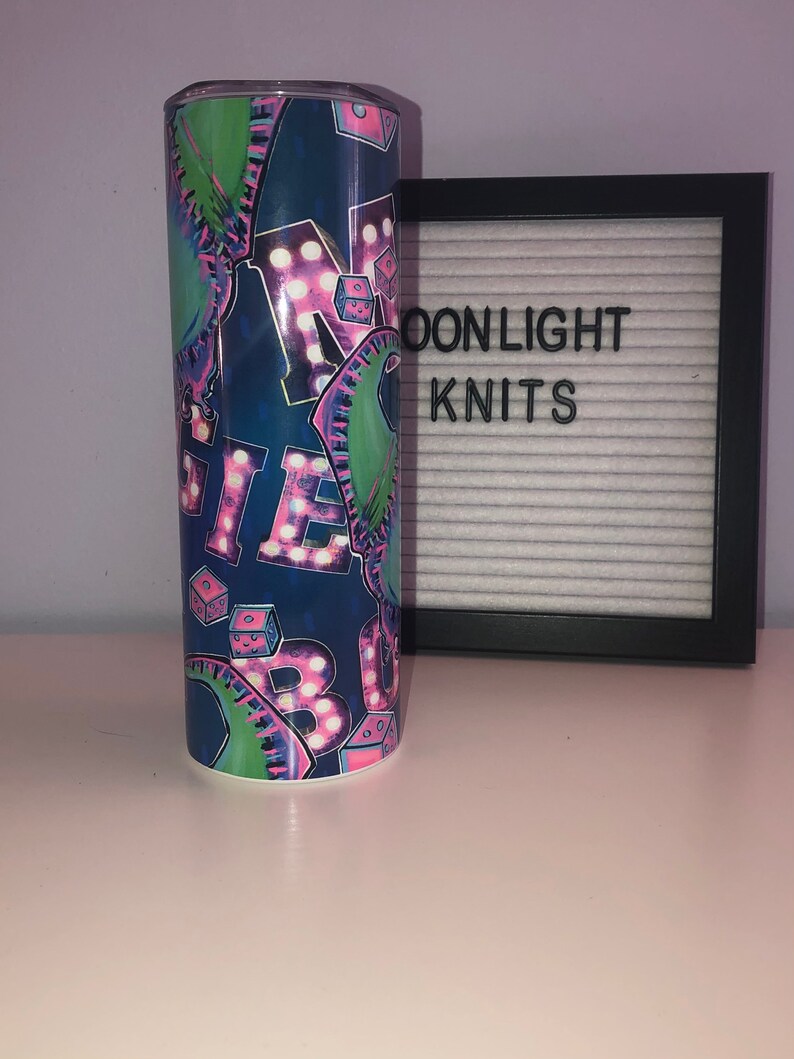 Puede incluir: Un vaso de acero inoxidable azul y verde con un dise&ntilde;o gr&aacute;fico rosa y blanco de la palabra "MAGIC" en luces de ne&oacute;n y dados.