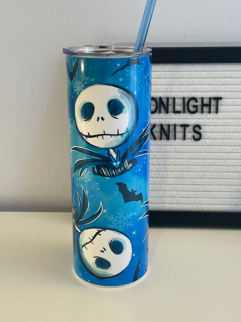 Może przedstawiać: Niebieski kubek termiczny ze stali nierdzewnej z białą pokrywką i słomką. Kubek ma powtarzający się wz&oacute;r postaci z kresk&oacute;wek z szytą buzią, nietoperzami i płatkami śniegu.