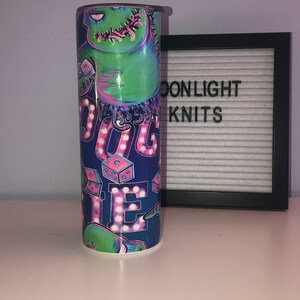 Puede incluir: Un vaso azul y verde con un gr&aacute;fico de un monstruo verde con acentos rosas y morados. El monstruo sostiene un dado y el texto "Boogie" est&aacute; escrito en luces rosas y blancas.