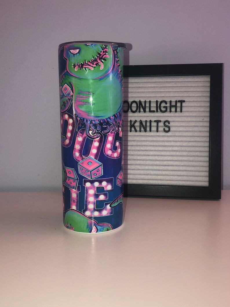 Puede incluir: Un vaso azul y verde con un gr&aacute;fico de un monstruo verde con acentos rosas y morados. El monstruo sostiene un dado y el texto "Boogie" est&aacute; escrito en luces rosas y blancas.