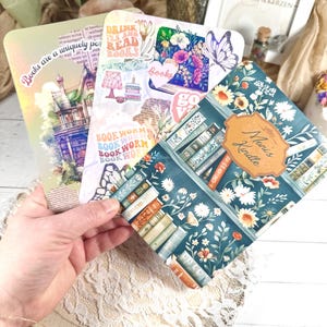 Könnte beinhalten: Eine Sammlung dekorativer Lesezeichen mit verschiedenen Designs. Ein Lesezeichen zeigt eine Illustration eines Gebäudes mit dem Text "Books are a uniquely portable magic". Ein anderes hat ein Blumenmuster mit dem Text "Drink tea and read books".