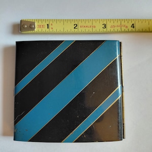 May include: A small, rectangular black and blue striped metal box. The box has diagonal stripes in black and blue, with gold trim. The box is approximately 3 inches wide.