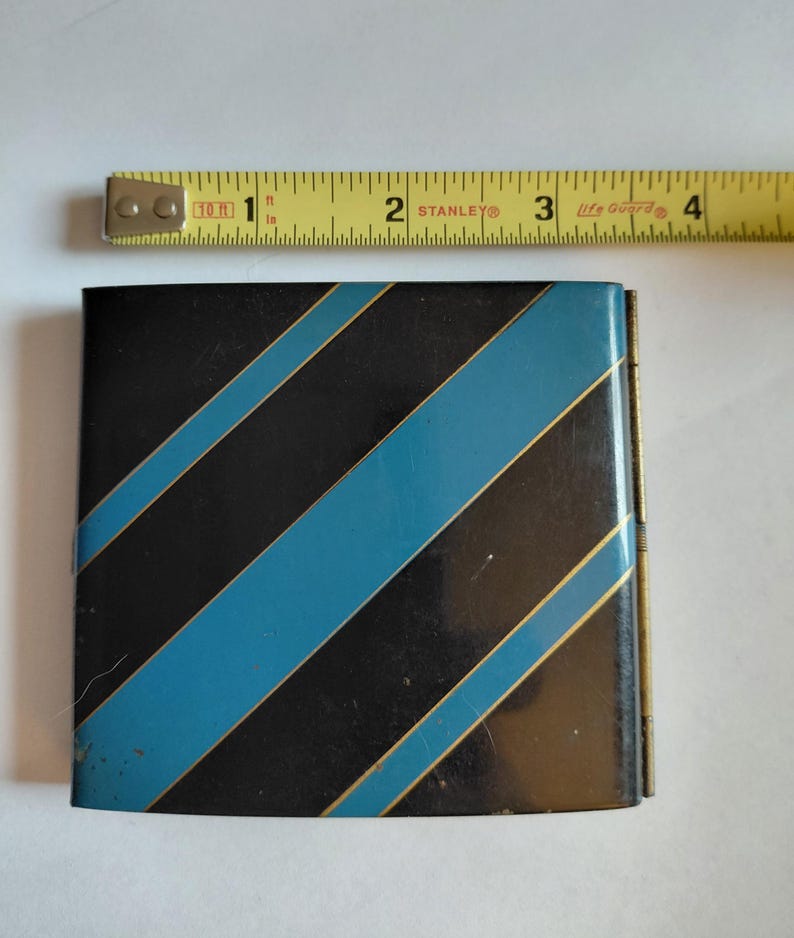 May include: A small, rectangular black and blue striped metal box. The box has diagonal stripes in black and blue, with gold trim. The box is approximately 3 inches wide.