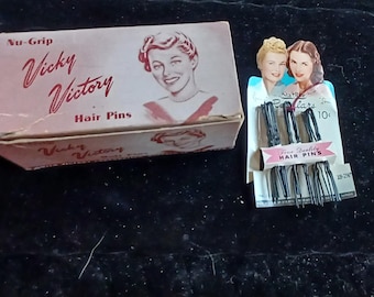 May include: A box of Vicky Victory No-Grip Hair Pins. The box is pink and white with a red and white logo. The box features a woman with blonde hair. The box is next to a package of hair pins. The package is white with a red and white logo. The package features two women with blonde hair. The package says "Starlite Bob Pins 10c" and "Fine Quality Hair Pins 25c".