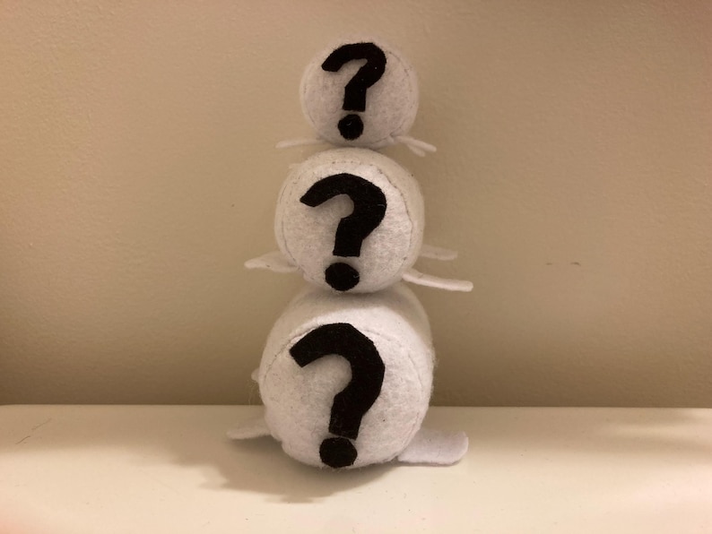 Three white, cylindrical felt plush toys stacked on top of each other, each with a large black question mark on the front.